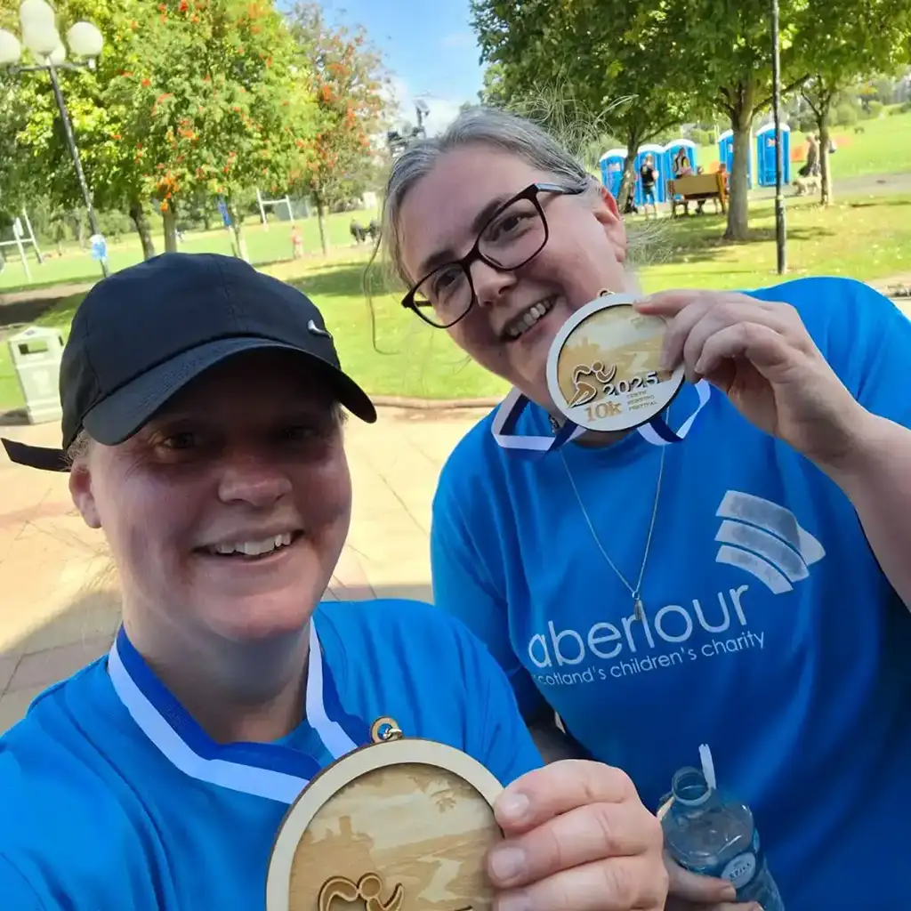 Denise wearing an Aberlour t-shirt and displaying fundraising medals
