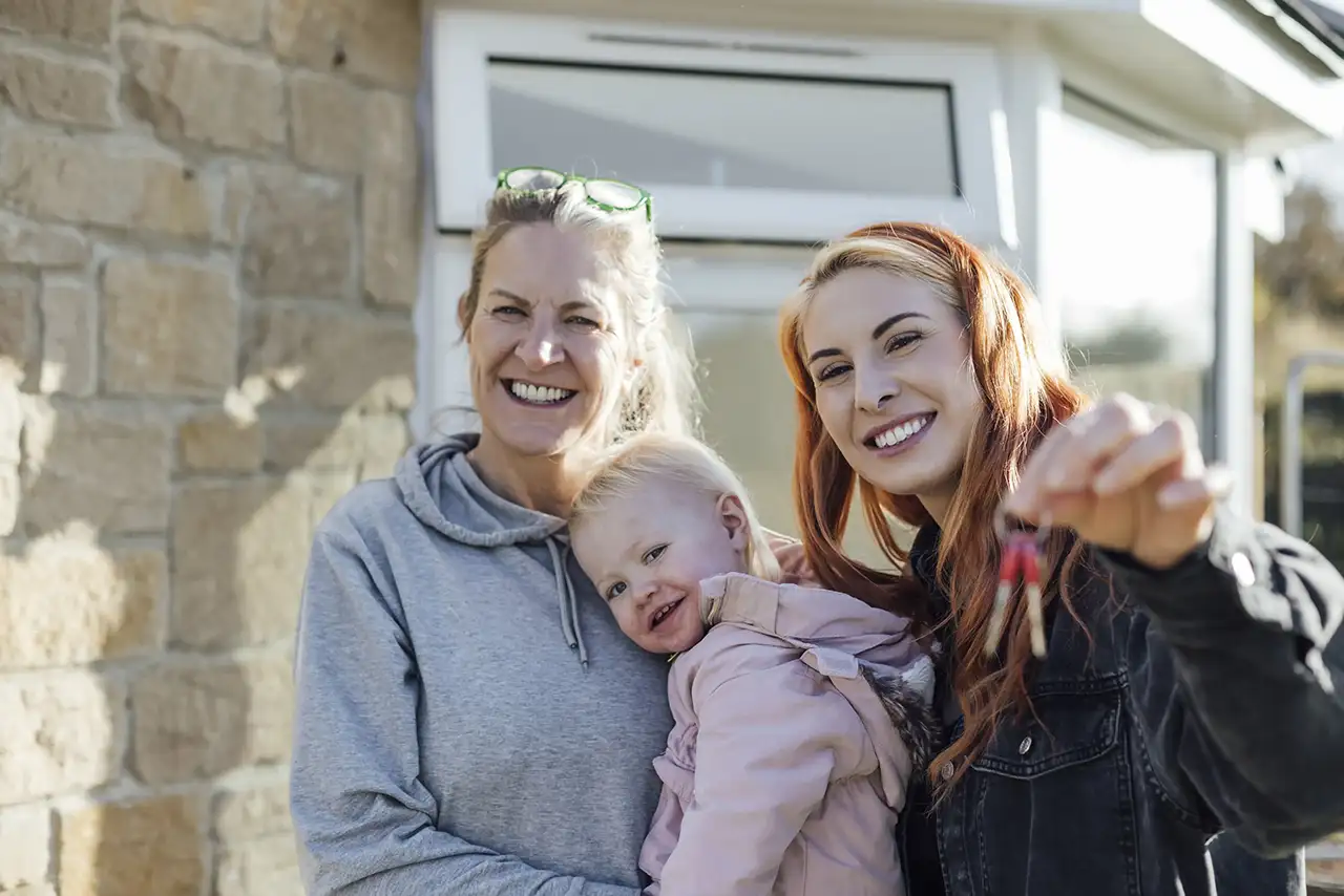 A family celebrating outside their new home, one of them holding up a set of house keys