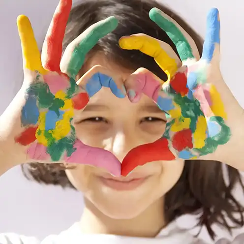 A child with brightly painted hands framing their face